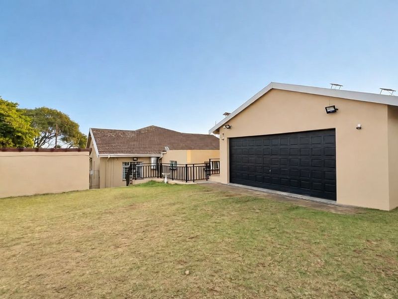Rear view of the property featuring a detached garage with a black sectional door, a grassed yard, and exterior security lighting.