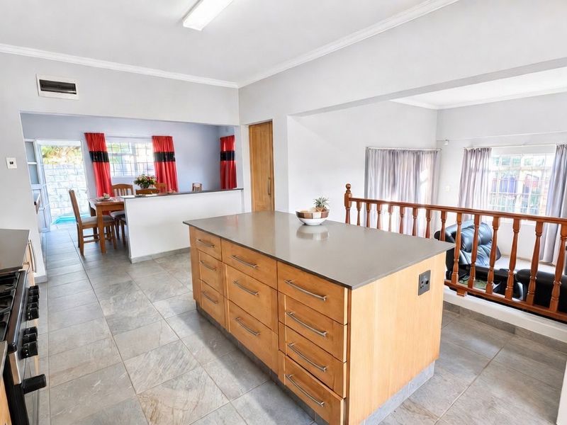 Spacious open-plan kitchen featuring a central island, stone countertops, gas cooktop, and tiled flooring, overlooking the adjacent dining and living areas.