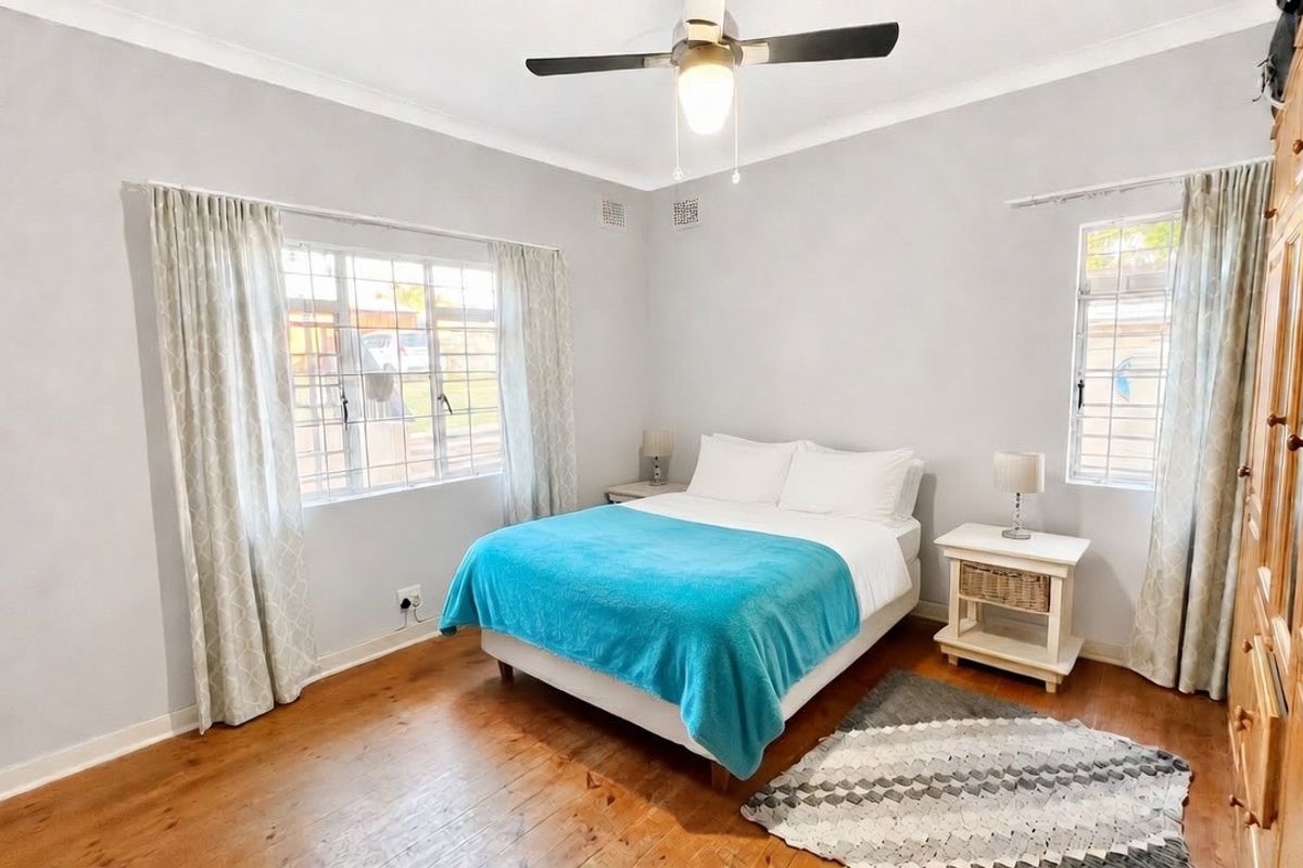 A well-lit bedroom featuring polished timber flooring, a ceiling fan, and built-in wooden wardrobes, offering a comfortable and functional living space.