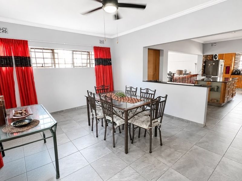 Open-plan dining area featuring tiled floors and a ceiling fan, flowing into a functional kitchen with wooden cabinetry and a central island.