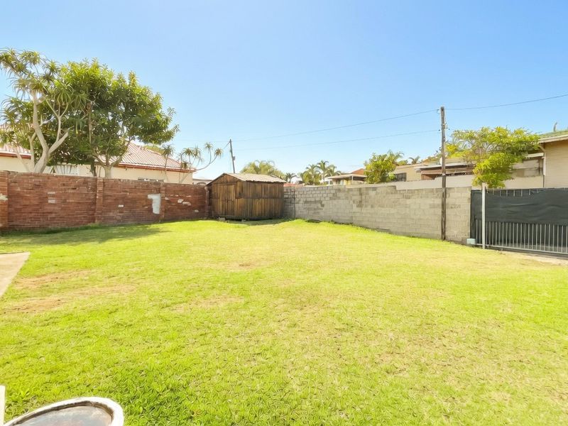 Spacious rear garden featuring a lawn, brick and concrete block boundary walls, and a wooden storage shed.