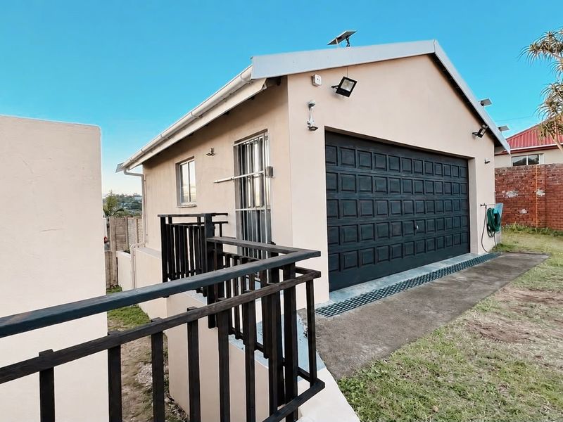 Exterior view of a detached garage featuring a black sectional door, security lighting, and a side entrance with security gate.