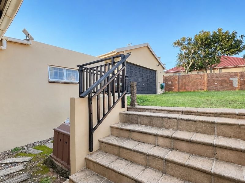 Rear exterior view featuring a tiled staircase with metal handrail, leading to a raised garden area and garage access.