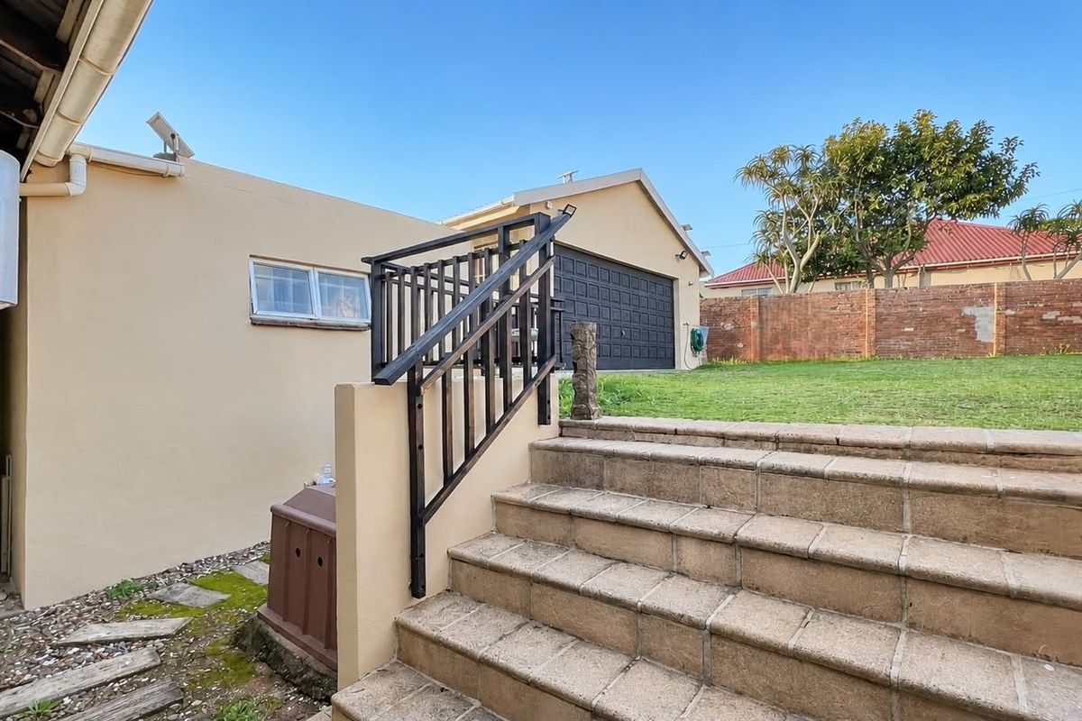 Rear exterior view featuring a tiled staircase with metal handrail, leading to a raised garden area and garage access.