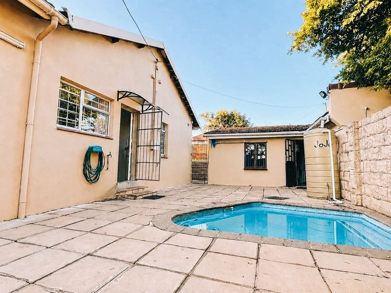 Rear exterior view featuring a paved patio area, a swimming pool, and a water storage tank adjacent to the main dwelling.