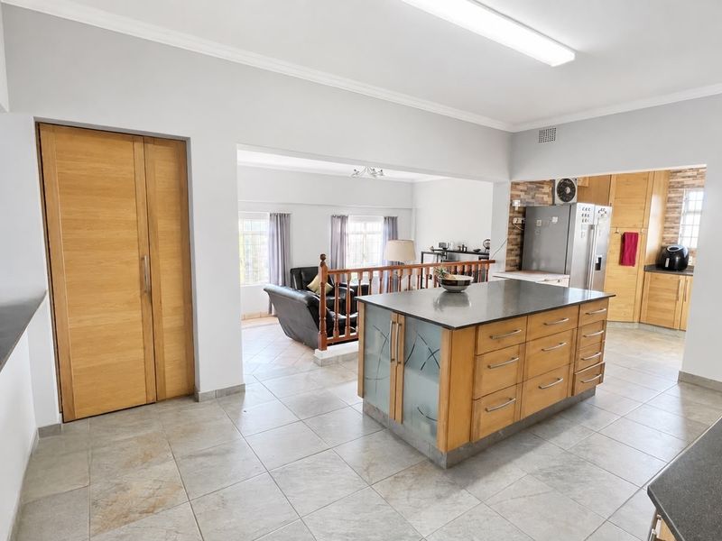 Spacious open-plan kitchen and living area featuring a central island with stone countertops, ample wooden cabinetry, and neutral tiled flooring throughout.