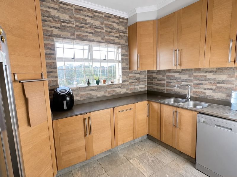 A functional kitchen featuring light wood cabinetry, stone-look tile backsplash, stone countertops, and integrated stainless steel sink with modern fixtures.