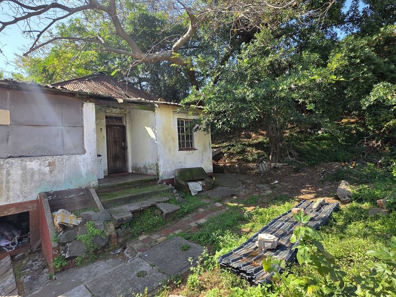 Front elevation of a dilapidated single-story dwelling showing significant wear to the exterior walls, roof, and surrounding grounds.