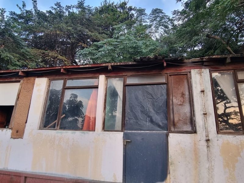Rear exterior view of a structure showing significant wear to the facade, roofline, and window frames, indicating a need for major maintenance or renovation.
