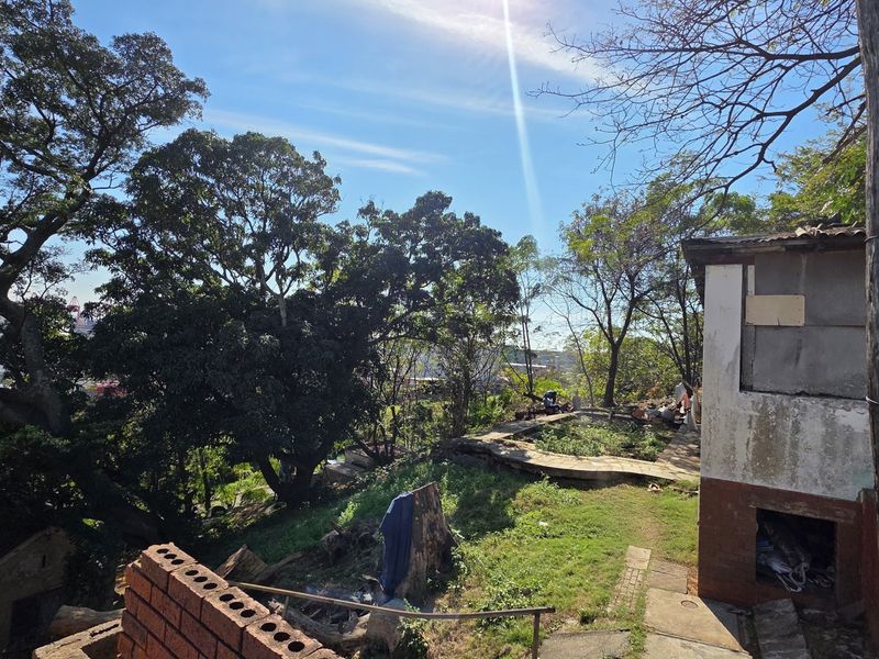 A view of the rear exterior area featuring mature trees, a concrete pathway, and a building structure showing significant signs of wear and deterioration.