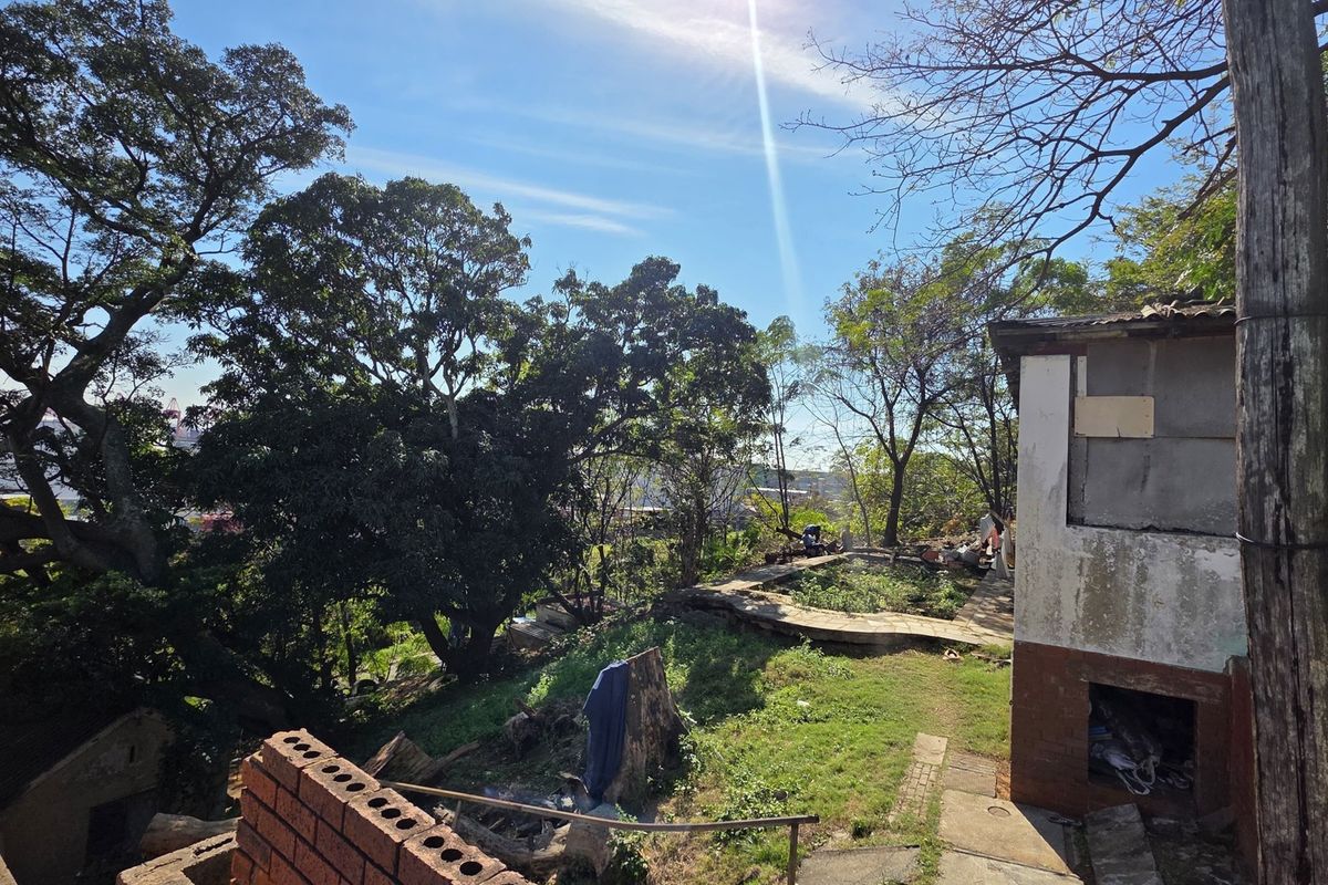 A view of the rear exterior area featuring mature trees, a concrete pathway, and a building structure showing significant signs of wear and deterioration.