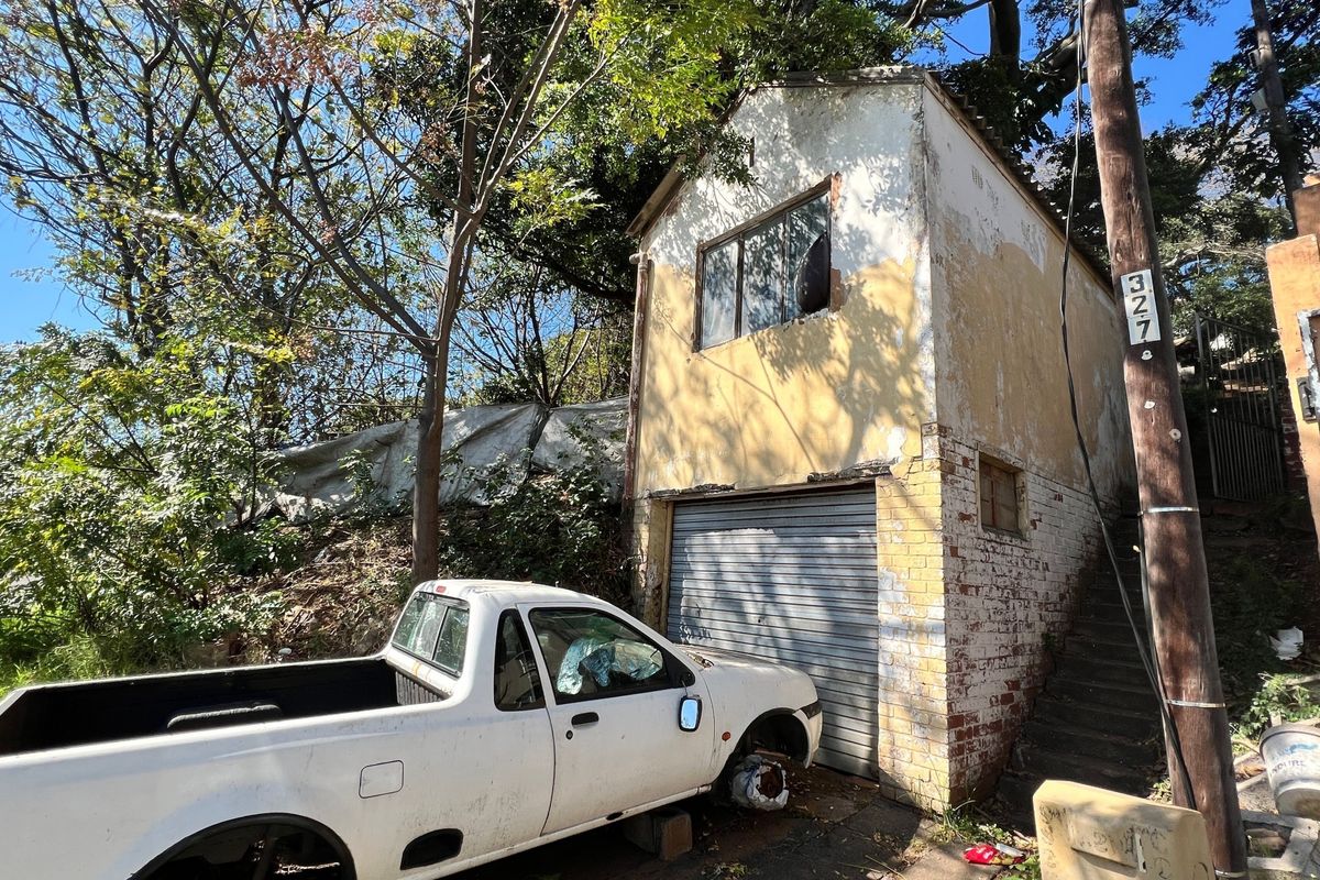 A detached garage structure showing significant signs of exterior wear, including peeling paint, damaged brickwork, and a broken window.