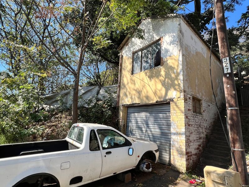 A detached garage structure showing significant signs of exterior wear, including peeling paint, damaged brickwork, and a broken window.