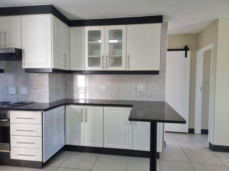 Modern kitchen featuring white cabinetry, dark granite countertops, built-in oven and hob, tiled backsplash, and a convenient breakfast bar.