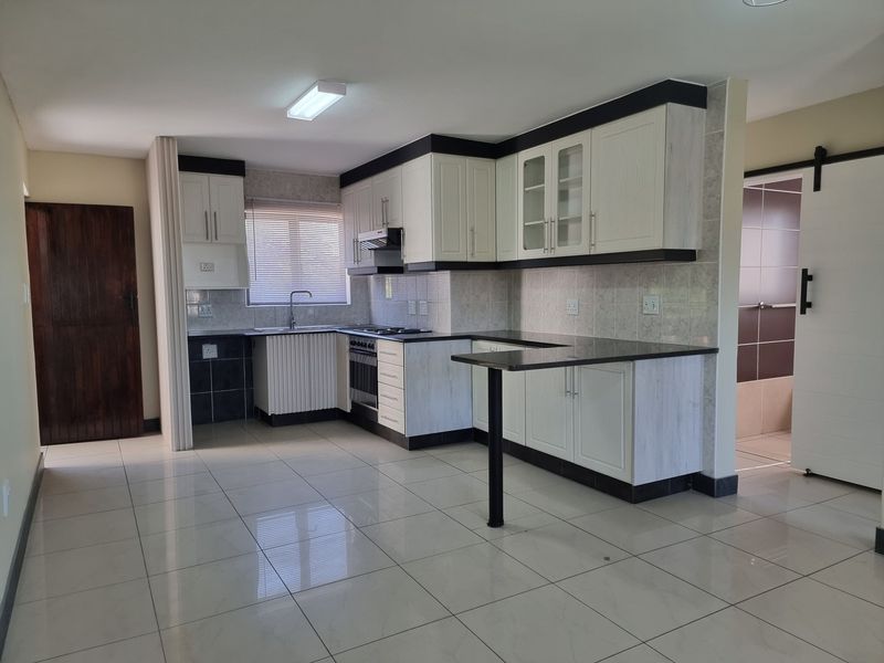 A clean, open-plan kitchen featuring white cabinetry, dark granite countertops, built-in appliances, and neutral ceramic floor tiles.
