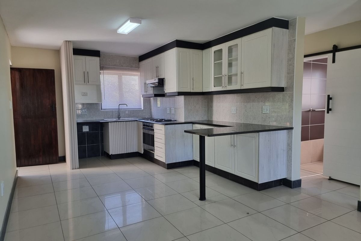 A clean, open-plan kitchen featuring white cabinetry, dark granite countertops, built-in appliances, and neutral ceramic floor tiles.