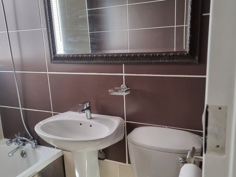 A functional bathroom featuring a pedestal basin, toilet, and bathtub with tiled walls and a wall-mounted mirror.