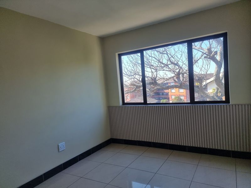 A bright, empty bedroom featuring tiled floors, modern vertical slat wall paneling, and a large window with an exterior view.