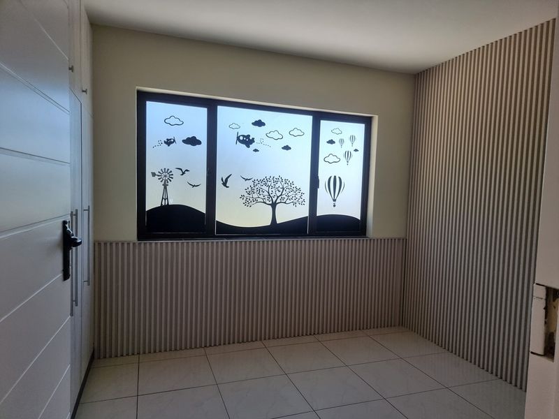 A clean, empty bedroom featuring modern slatted wall paneling, built-in cupboards, and tiled flooring with a decorative window film.