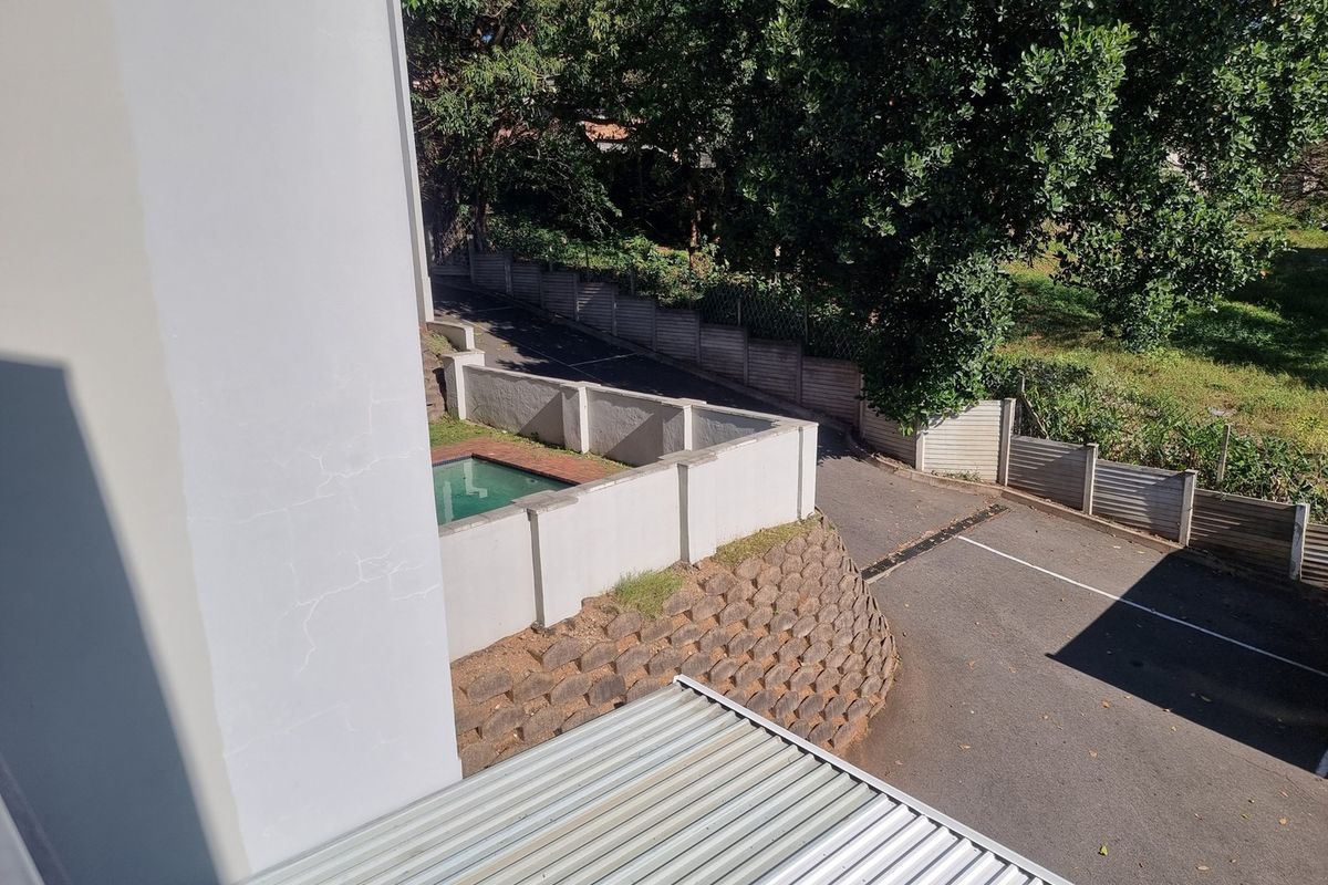 An elevated view of the property exterior showing a paved driveway, boundary walls, and a section of corrugated metal roofing.
