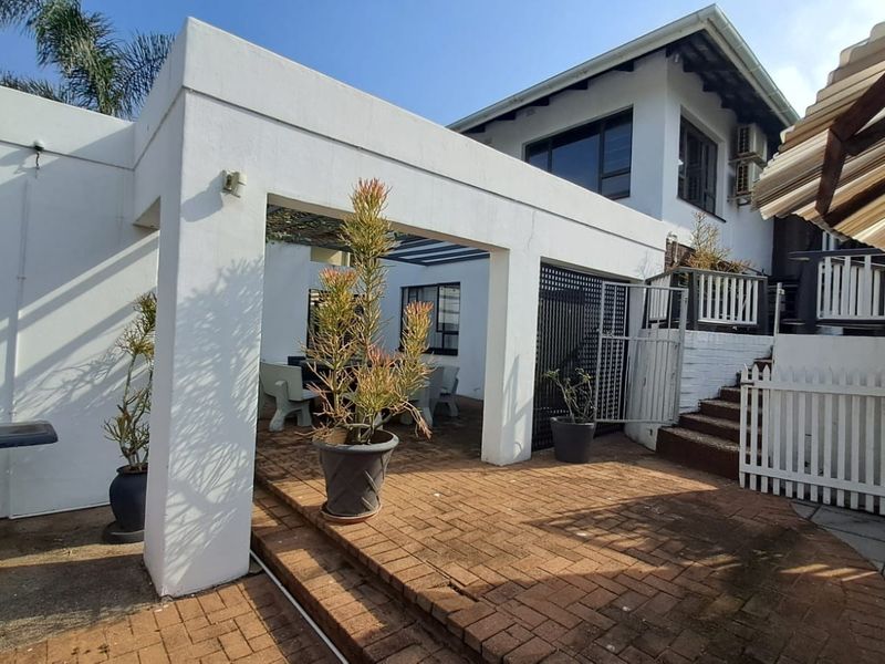 A spacious outdoor patio area featuring brick paving, a covered structure, and stairs leading to the upper level of the property.