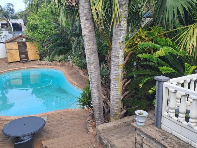 Outdoor pool area featuring a swimming pool, brick paved surround, and a wooden storage shed set within a landscaped garden.
