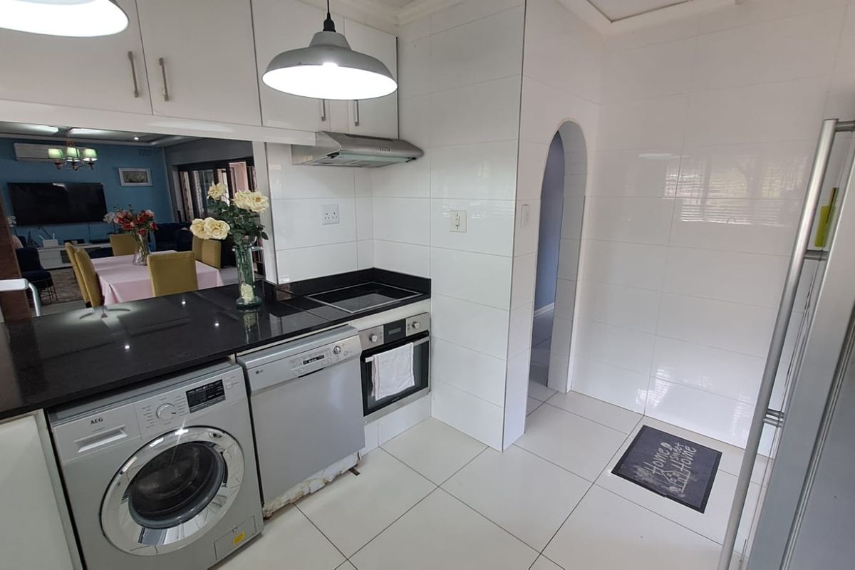 Modern kitchen featuring black granite countertops, built-in oven, electric hob, extractor fan, and tiled finishes, with an open-plan layout connecting to the dining area.