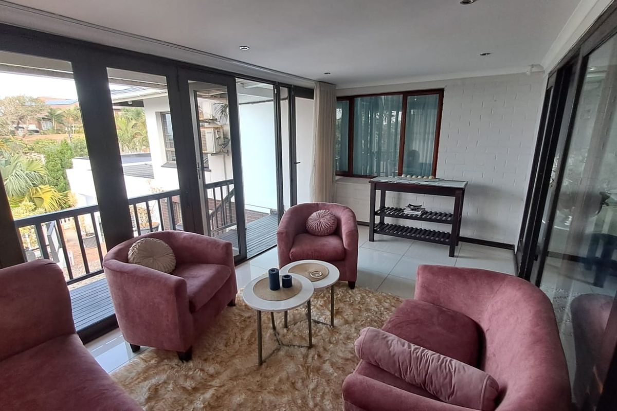Bright living area featuring large sliding glass doors that open to an outdoor balcony, complemented by tiled flooring and a textured painted brick wall.