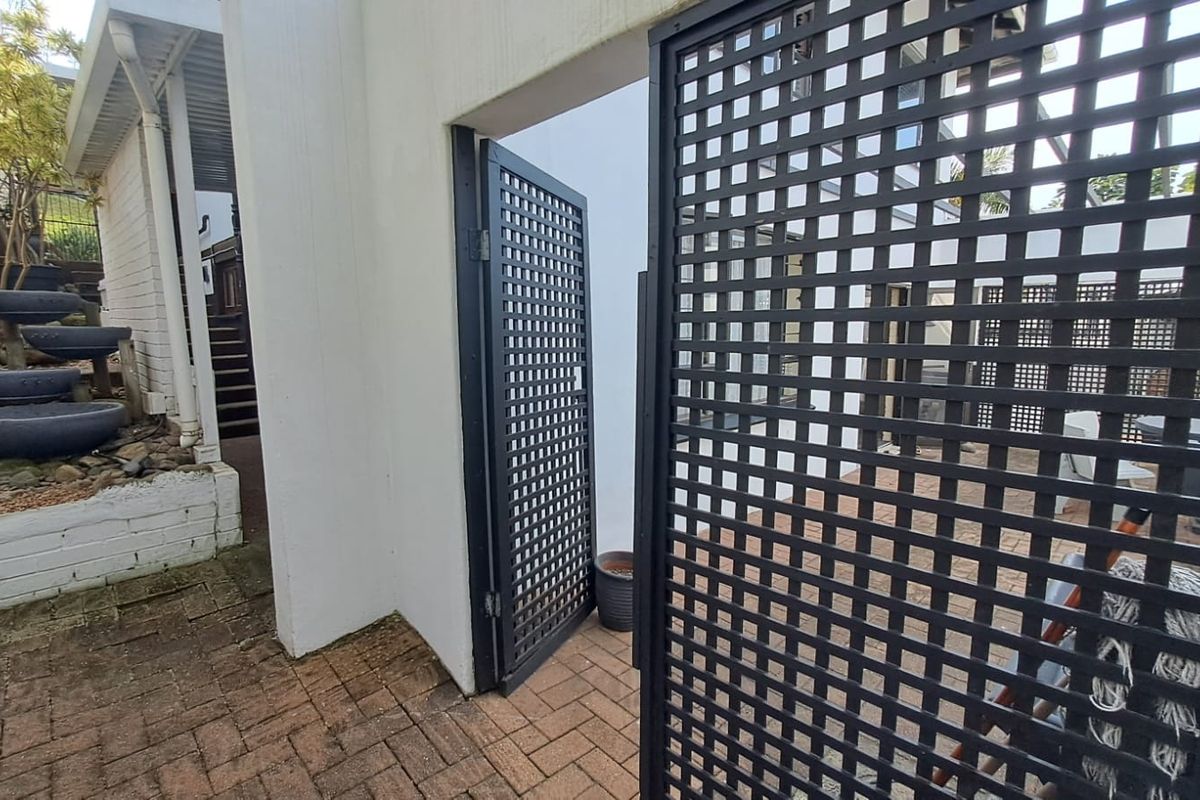 A rear exterior view featuring brick paving, a metal lattice gate, and a tiered garden area with a staircase leading to the upper level.