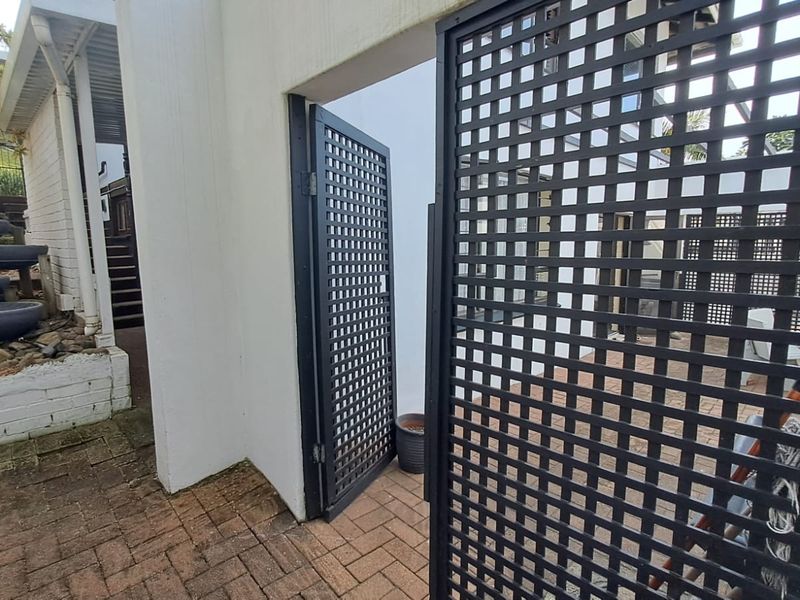 A rear exterior view featuring brick paving, a metal lattice gate, and a tiered garden area with a staircase leading to the upper level.