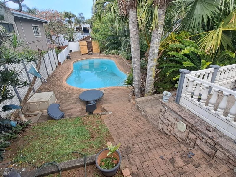 Outdoor pool area featuring a swimming pool, brick paved surround, and a raised terrace with a decorative balustrade.