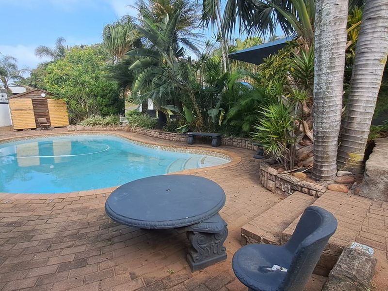 Outdoor pool area featuring a swimming pool, brick paved surround, and established garden landscaping with a small storage shed.