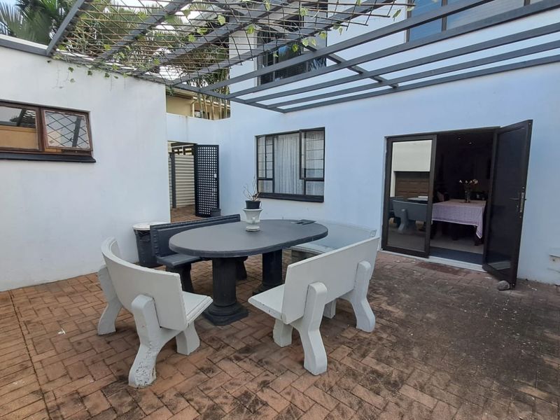 A paved outdoor patio area featuring a metal pergola structure, providing a functional space for outdoor dining and entertaining.