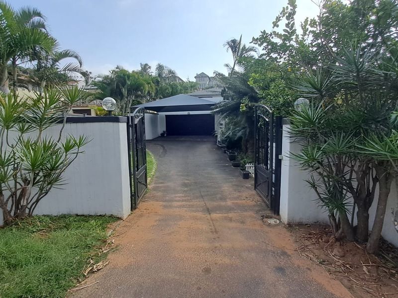 Front entrance view featuring a gated driveway leading to a covered carport and garage area with established perimeter walls and landscaping.