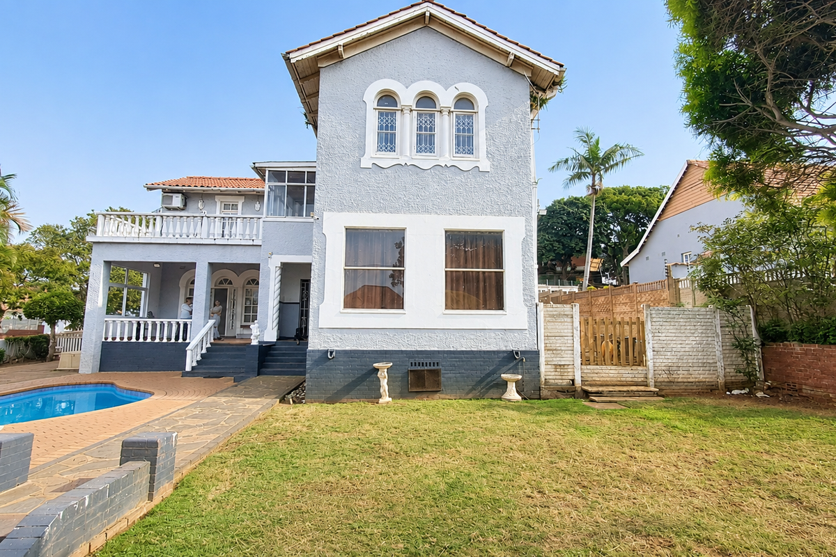 Rear view of a multi-story house featuring a swimming pool, paved patio area, balcony, and a private garden with boundary walling.