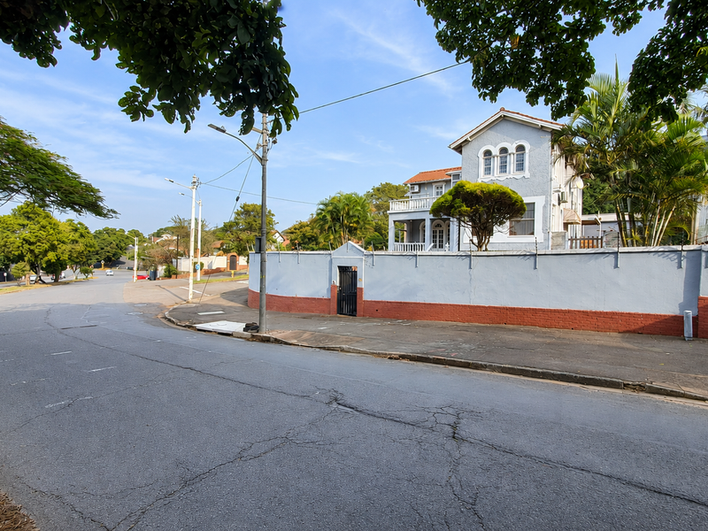 Street view of a residential property featuring a perimeter wall, gated entrance, and a multi-story house with a tiled roof and terrace.