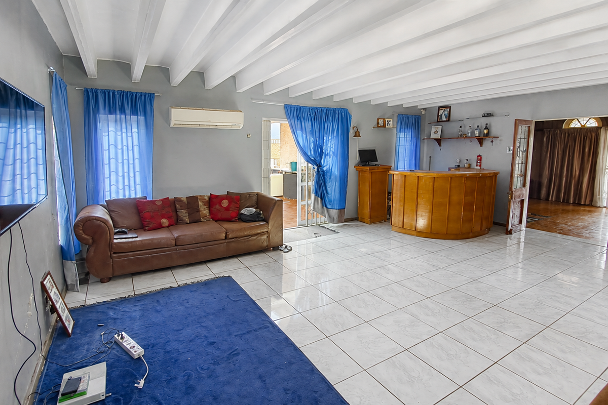 Spacious living area featuring exposed beam ceilings, ceramic tile flooring, and a built-in bar counter, offering a versatile layout for entertainment.
