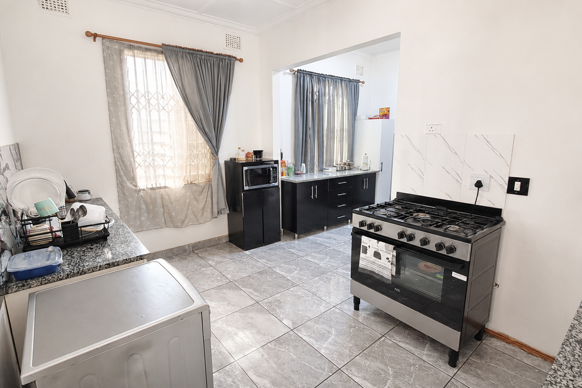 A functional kitchen featuring granite countertops, dark cabinetry, a gas stove with oven, and tiled flooring with a connected secondary prep area.