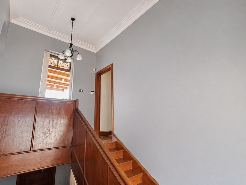 A bright, well-maintained hallway featuring a classic wooden staircase with a matching balustrade, decorative ceiling cornicing, and a charming stained glass window.
