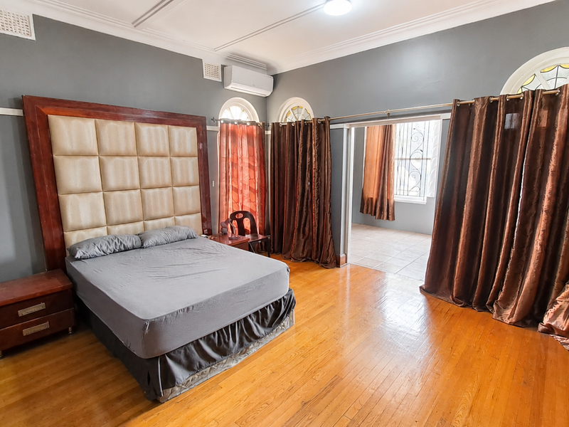 Spacious bedroom featuring hardwood flooring, split-system air conditioning, and arched windows, with an adjoining room accessible through a wide opening.