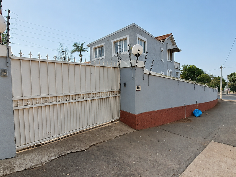 Front exterior view of the property featuring a secure sliding gate, perimeter wall with electric fencing, and a paved driveway.