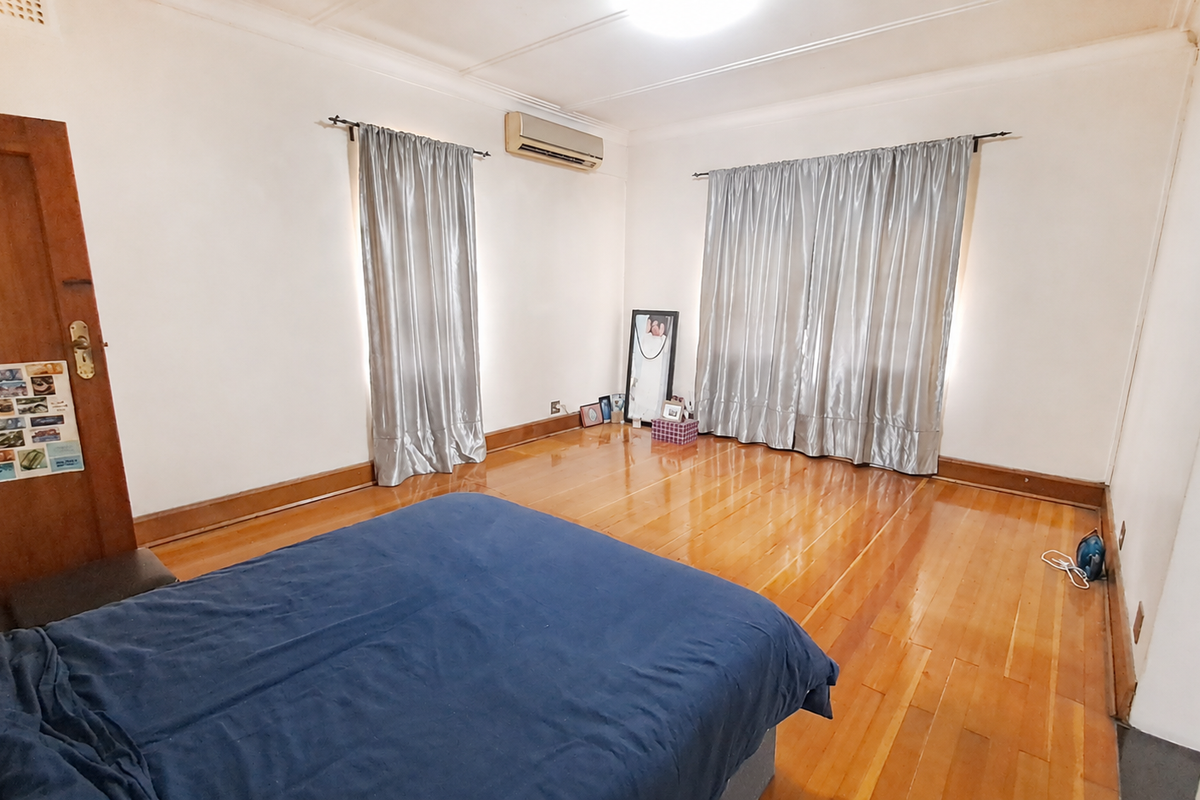 Spacious bedroom featuring polished hardwood flooring, a wall-mounted split-system air conditioner, and classic timber door finishes.