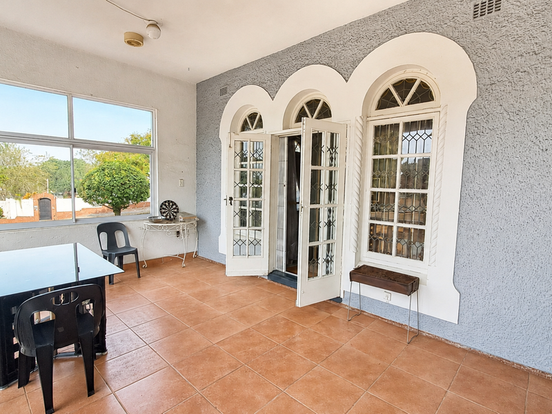 A covered patio area featuring tiled flooring, arched french doors, and large windows, providing a bright and functional outdoor living space.