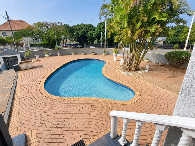 Outdoor pool area featuring a kidney-shaped swimming pool surrounded by brick paving and a perimeter boundary wall.