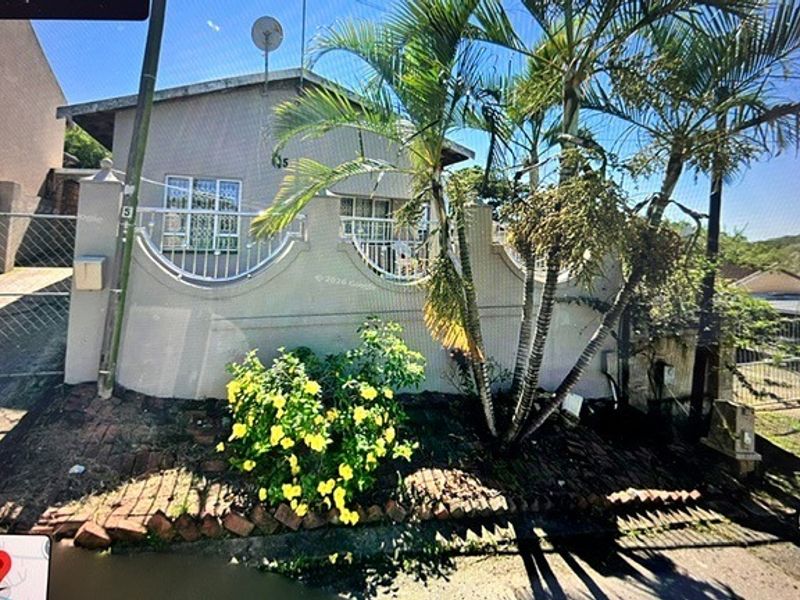 Front exterior view of the property featuring a perimeter wall, security gate, and established garden area.