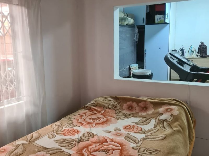 A bedroom featuring a window looking through to an adjacent room, with tiled flooring and a security gate on the exterior window.
