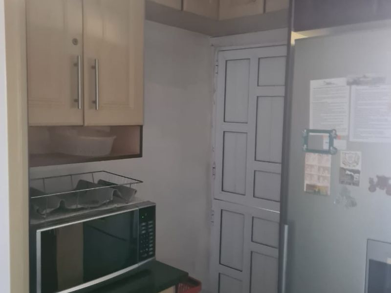A compact kitchen area featuring light wood-toned built-in cabinetry, dark countertops, and a built-in microwave, providing functional storage and preparation space.