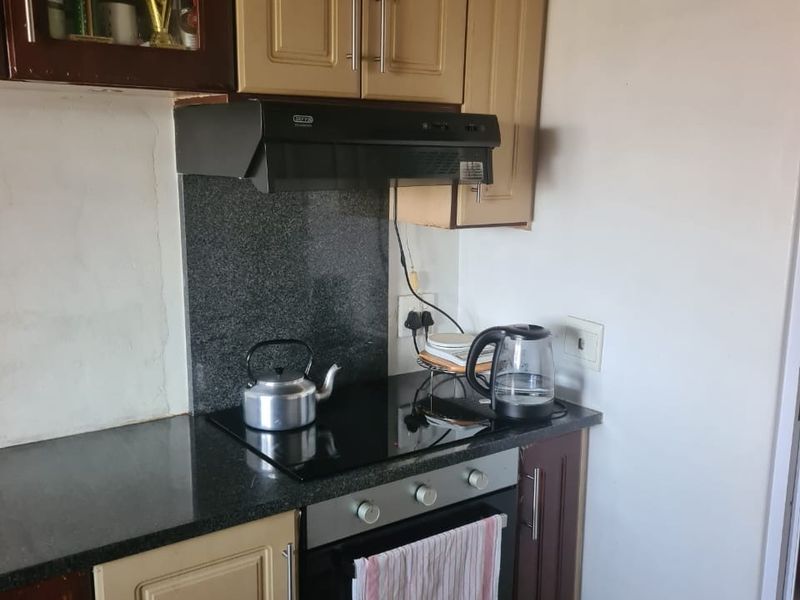 A functional kitchen area featuring built-in cabinetry, a granite countertop with matching splashback, and integrated cooking appliances including an oven and extractor fan.