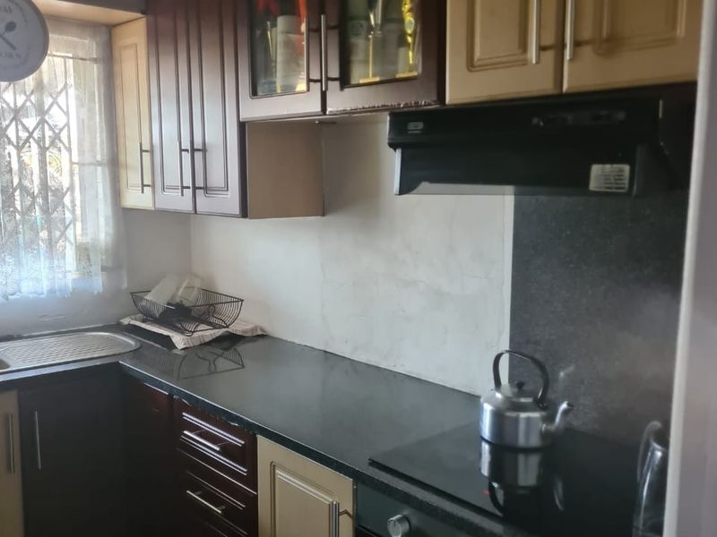 A functional kitchen featuring two-tone cabinetry, granite countertops, a built-in oven with hob, and an extractor fan, with an unfinished wall area.