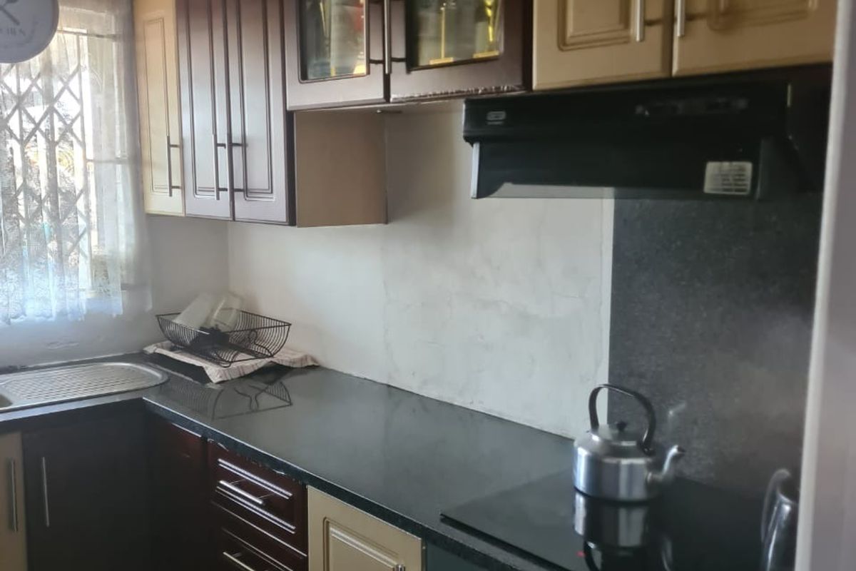 A functional kitchen featuring two-tone cabinetry, granite countertops, a built-in oven with hob, and an extractor fan, with an unfinished wall area.